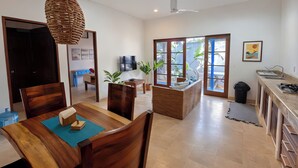 A spacious living area with a dining table, chairs, a TV, and a view of the outdoors through large sliding doors. - Spacious 2BR w/ Pool •  Walk to Beach & Town • Quiet area (Sayulita)
