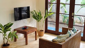 A living room with a television, a sofa, a table, and potted plants. - Spacious 2BR w/ Pool •  Walk to Beach & Town • Quiet area (Sayulita)