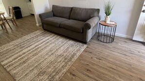 Ein Wohnzimmer mit grauem Sofa, einem Streifenmuster-Teppich, einem kleinen runden Tisch mit einer Pflanze und zwei Wandbildern.