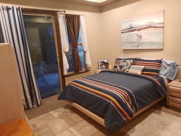 Une chambre à coucher avec un lit, une fenêtre avec des rideaux, un tableau au mur et une petite table avec une lampe.