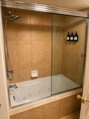 Une douche à l’italienne avec une porte en verre, une baignoire et trois bouteilles de shampoing fixées au mur.