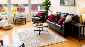 A modern living room with a black leather sofa, a round coffee table, a white rug, and a large window with a view of buildings. - NEW LISTING Charming 2/2 loft/heart of downtown. 5 min walk Convention Center (Denver)