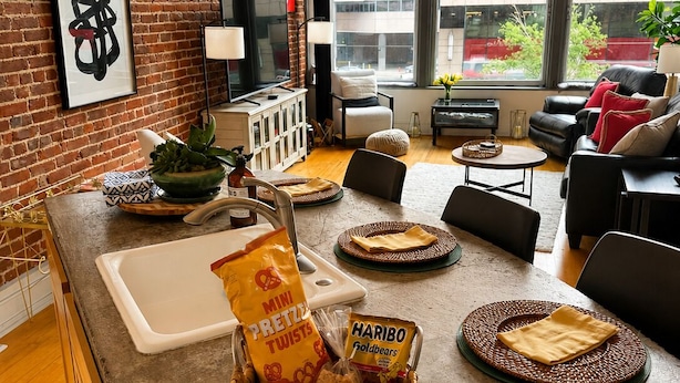 A modern kitchen with a brick wall, a large window, and a dining area with a sofa and chairs. - NEW LISTING Charming 2/2 loft/heart of downtown. 5 min walk Convention Center (Denver)
