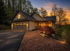 A two-story house with a garage, surrounded by trees and a gravel driveway.