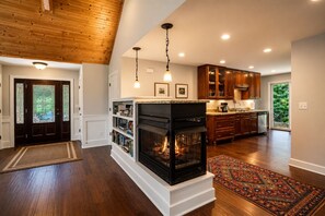 A spacious living area with a fireplace, wooden flooring, and a view of the outdoors.