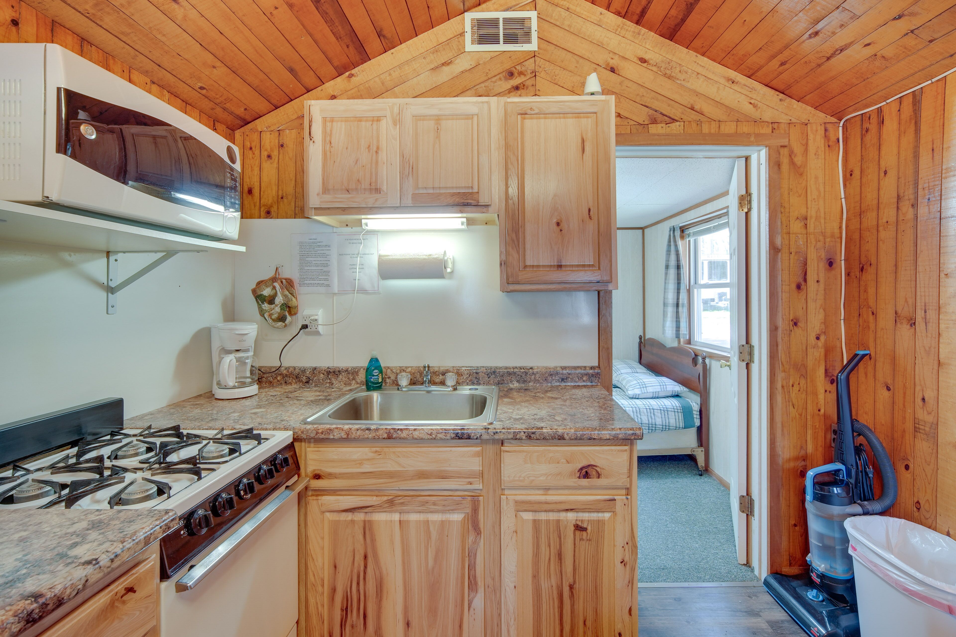 A compact kitchen with wooden cabinets, a gas stove, a sink, and a coffee maker.