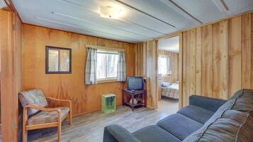 A room with wooden walls, a sofa, a chair, a television on a wooden stand, and a small table.