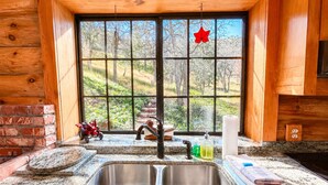 A kitchen with a double sink, a window with a view of trees, and a red leaf decoration. - Bodfish Ranch/ sleeps 14 / secluded on 3.5 acres (Bodfish)