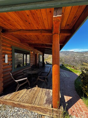 A log cabin with a covered patio, outdoor seating, and a view of the surrounding landscape.