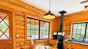 A wooden cabin interior with a round dining table, chairs, a built-in grill, and large windows. - Bodfish Ranch/ sleeps 14 / secluded on 3.5 acres (Bodfish)