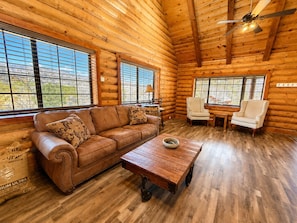 A log cabin interior with a leather sofa, a wooden coffee table, and two white armchairs.