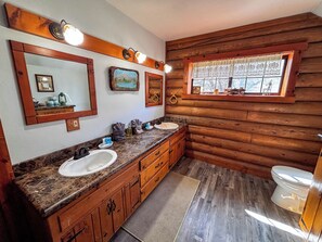 Een badkamer in chaletstijl met houten accenten, een dubbele wastafel, een badkamermeubel en een raam met uitzicht.