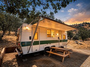 Una caravana antigua con zona de dormitorio cubierta, mesa de comedor y pequeña cocina.