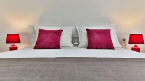 A bed with white bedding and two red pillows, flanked by two red lamps.