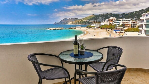 A balcony with a table and chairs overlooking a beach and buildings.