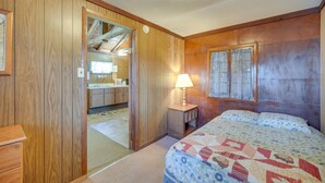 A bedroom with a wooden headboard, a bed with a quilt, a nightstand with a lamp, and a door leading to a bathroom. - Stone Lake Cabin w/ Private Deck & Fire Pit! (Stone Lake)