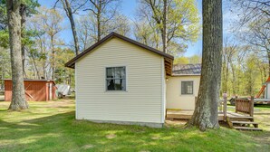 A small, single-story building with a gabled roof, surrounded by trees and grass. - Stone Lake Cabin w/ Private Deck & Fire Pit! (Stone Lake)