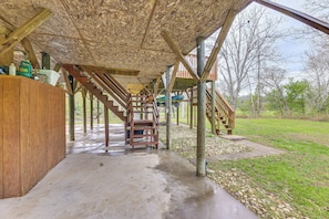 Un espacio al aire libre cubierto, con suelo de concreto, escaleras de madera y una terraza de madera.