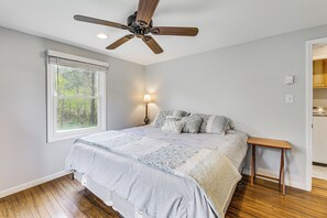 Een slaapkamer met een bed, een plafondventilator, een raam en een nachtkastje.