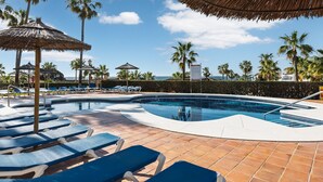 Zona de piscina con sillones de descanso, palmeras y cielo despejado.
