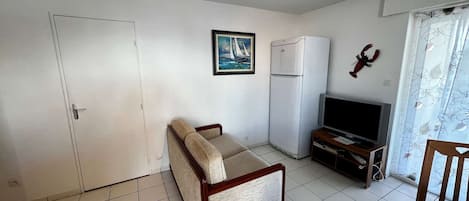 Una habitación pequeña y ordenada con un sofá, un televisor, un refrigerador y una puerta.