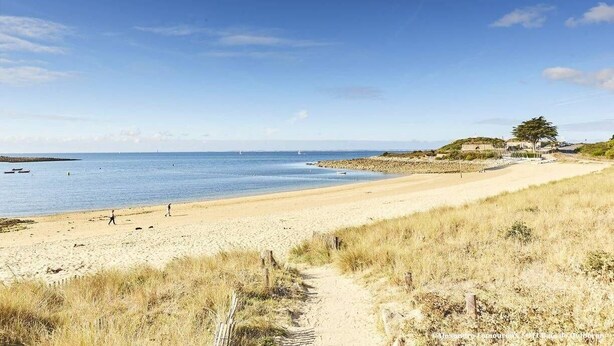 A beach with a clear path leading to the water, a few people walking, and a building with a tree on the right. - St Philibert - 2-room apartment - 32m² - WIFI (ST PHILIBERT)