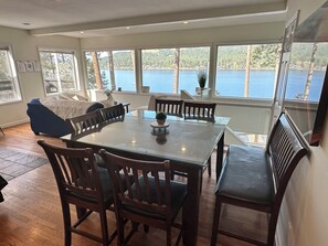 A dining area with a glass table, wooden chairs, and a view of a lake. - Beautiful Liberty Lake Waterfront House (Liberty Lake)