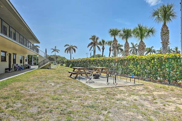 Un patio con mesas y sillas de picnic, rodeado de palmeras y un seto.
