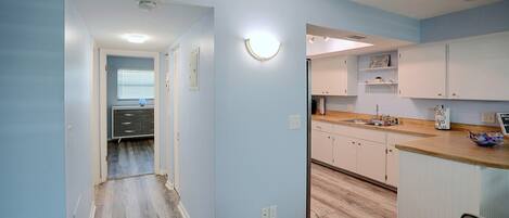 A modern kitchen with light blue walls, wooden flooring, and white cabinetry.