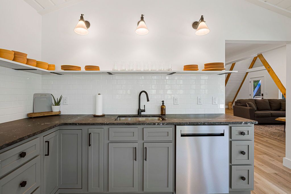 A modern kitchen with grey cabinets, a stainless steel dishwasher, and a countertop with orange plates and glasses.