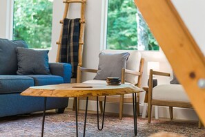 A cozy living room with a blue sofa, a wooden coffee table, and a chair with a plaid throw.