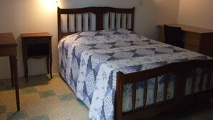 A bedroom with a wooden bed, two bedside tables, a patterned bedspread, and wall-mounted lamps.