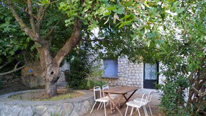 A rustic outdoor seating area with a stone wall, a tree, and a table with chairs.