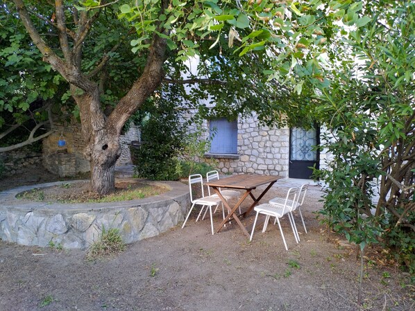 Un espacio de estar al aire libre rústico, con pared de piedra, un árbol y una mesa con sillas.
