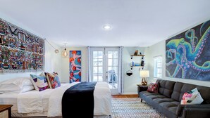 Un dormitorio con cama, sofá, alfombra estampada y un cuadro abstracto grande en la pared.