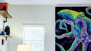Una sala de estar con una lámpara moderna, un cuadro de un pulpo colorido, un sofá oscuro y un tapete estampado.