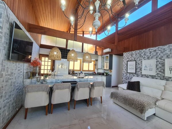 A modern kitchen with a central island, pendant lights, and a dining area with chairs.