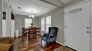 A dining area with a wooden table and chairs, a tufted armchair, and a patterned rug.