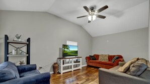 A living room with a TV, two sofas, a ceiling fan, and a wooden floor.