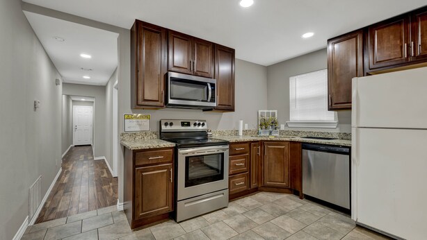 A kitchen with wooden cabinets, stainless steel appliances, and a tiled floor.