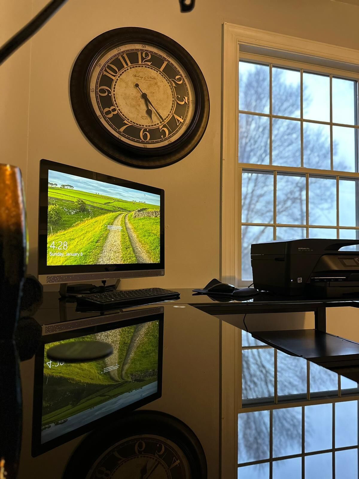 A room with a desk, two monitors, a clock, and a printer.