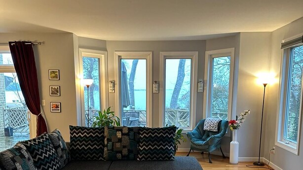 A modern living room with a sectional sofa, ottomans, and a view of a deck through large windows. - Relaxing Luxurious Waterfront in Hampton  (Hampton)