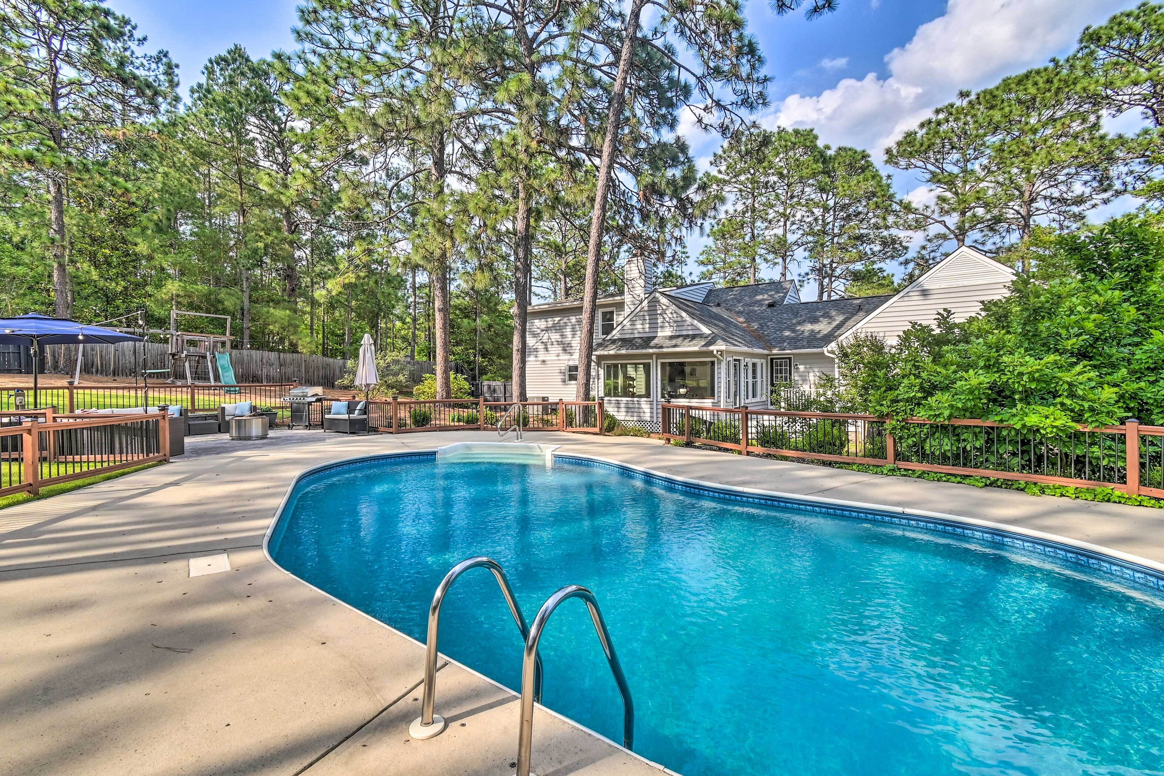 A swimming pool with a wooden deck, surrounded by a wooden fence and trees.