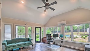 A spacious room with a green sofa, a black office chair, and a large window overlooking a backyard with a pool. - Peaceful Southern Pines Home w/ Pool + Yard! (Southern Pines)