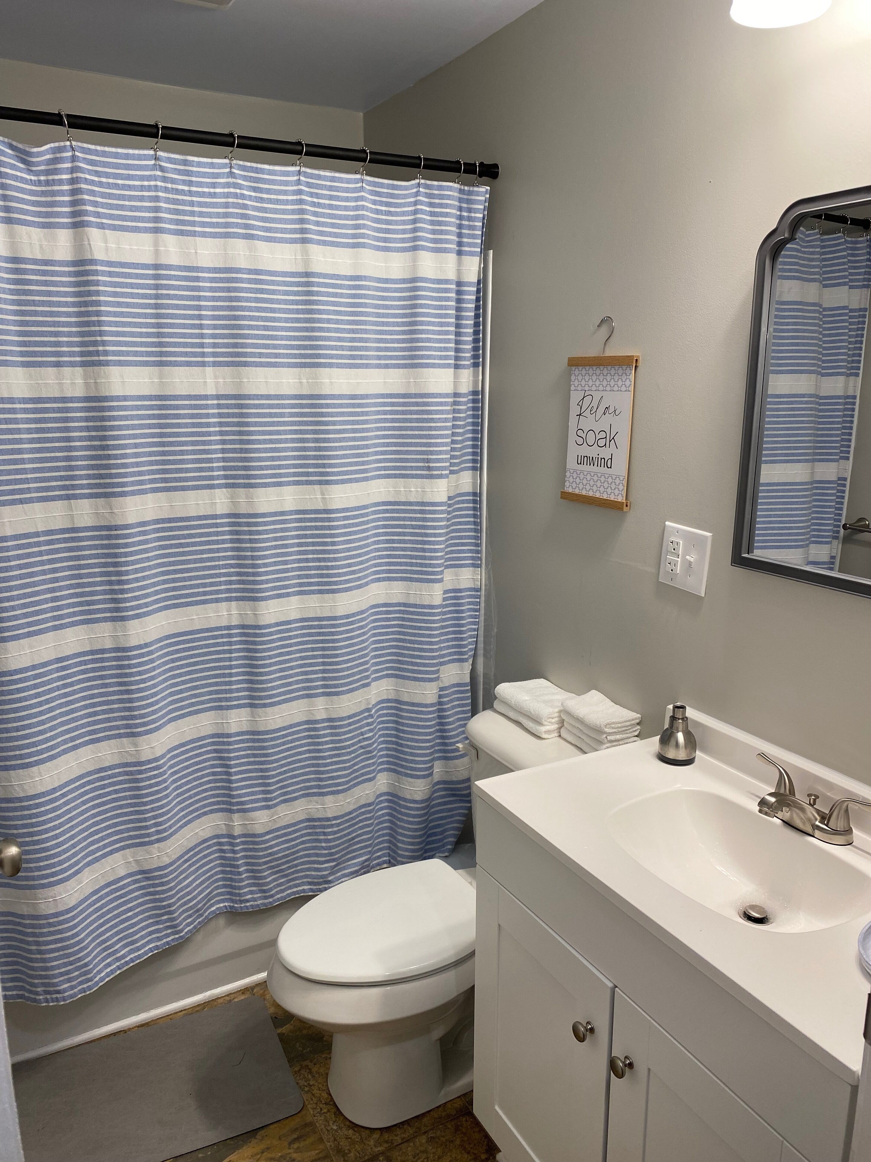 A bathroom with a striped shower curtain, a toilet, a sink with a mirror, and a towel rack.