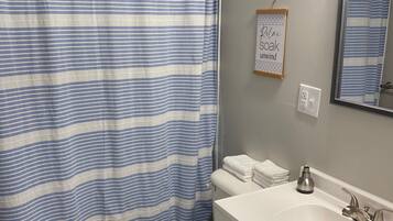 A bathroom with a striped shower curtain, a toilet, a sink with a mirror, and a towel rack.