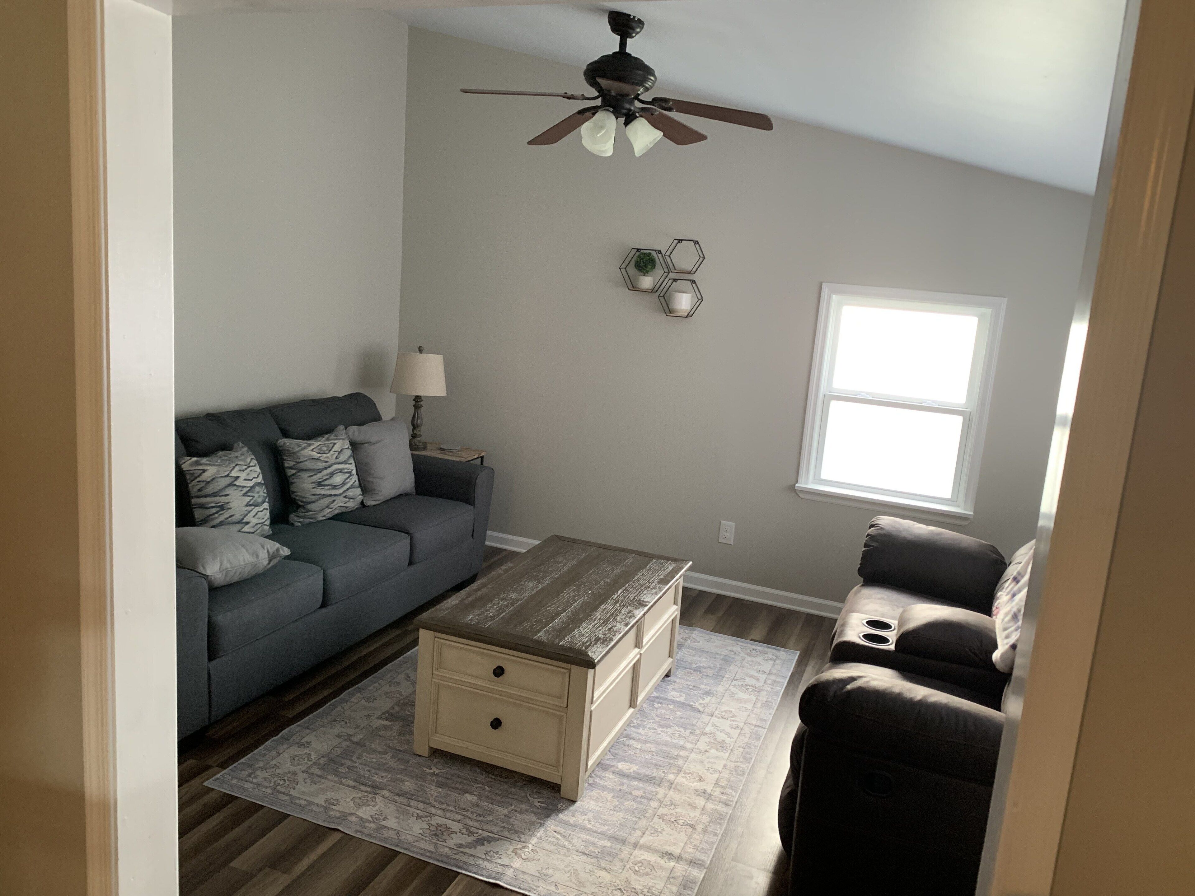Ein Wohnzimmer mit grauem Sofa, einem Holztisch und einem Deckenventilator.
