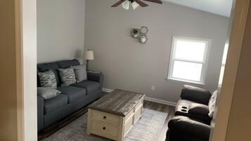 Ein Wohnzimmer mit grauem Sofa, einem Holztisch und einem Deckenventilator.