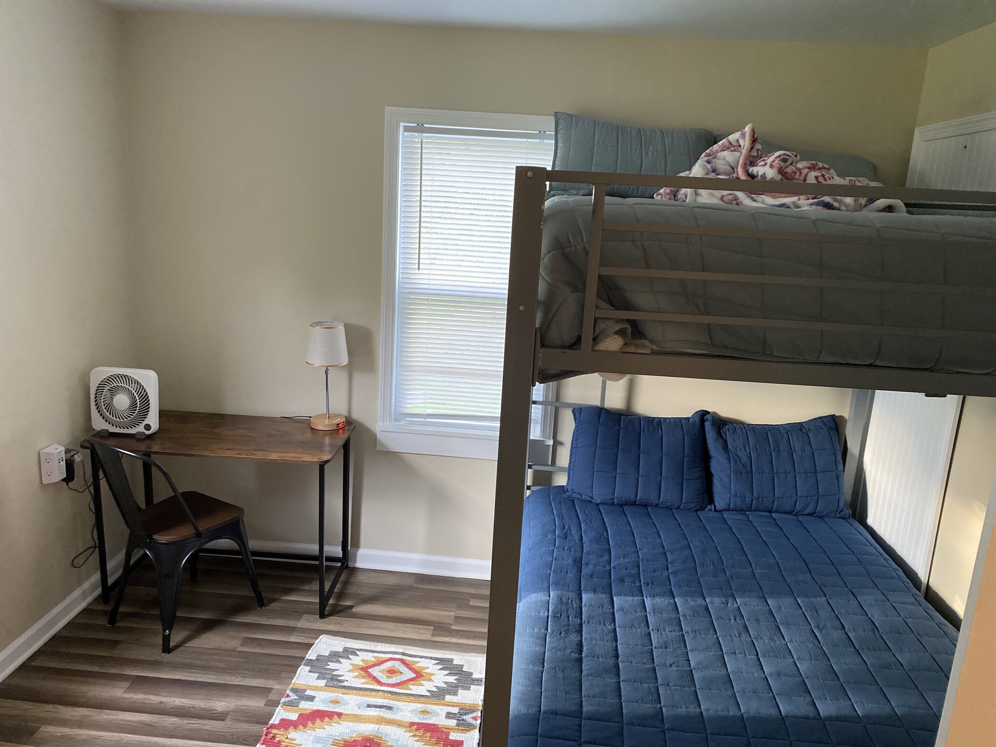 A bunk bed room with a desk, chair, and a patterned rug.