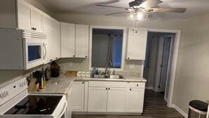 Cozinha com armários brancos, micro-ondas, fogão, pia e ventilador de teto.
